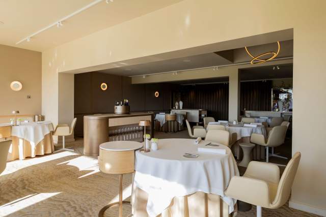 Une salle de restaurant élégante et contemporaine, équipée de tables rondes et dotée d'un espace bar intégré.