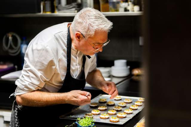 Un chef en cuisine prépare avec soin une série de bouchées.