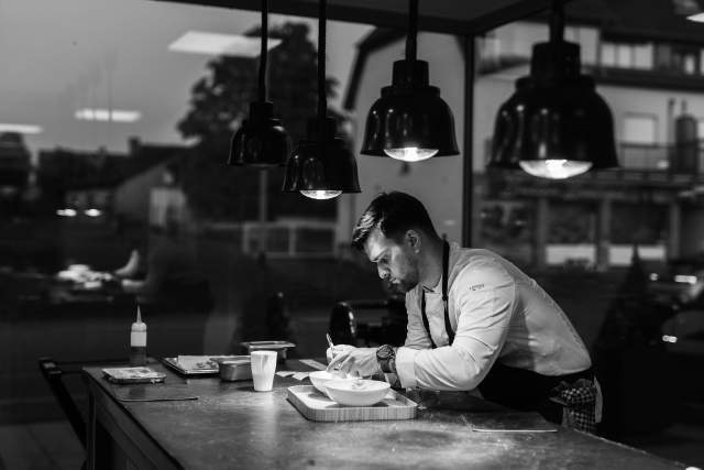 Un chef en cuisine, concentré sur la finition d'un plat, dans une élégante ambiance en noir et blanc.