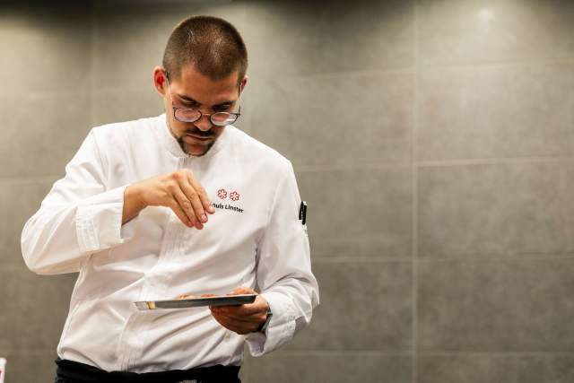 Un chef en tenue blanche en train de préparer un plat.
