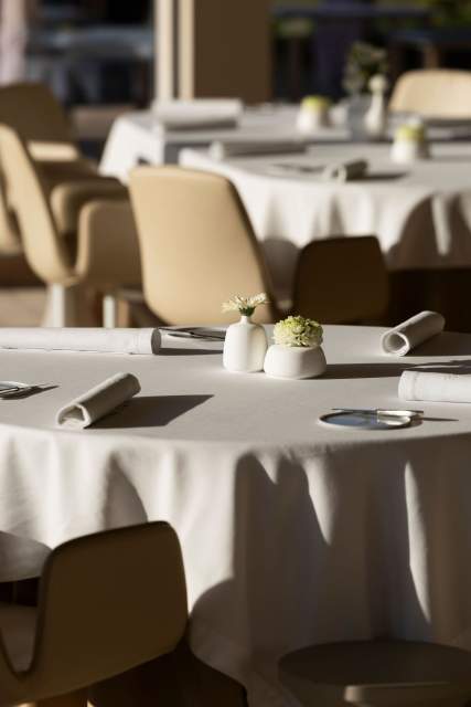 Une table de restaurant élégamment dressée, avec une nappe blanche et une composition florale minimaliste.