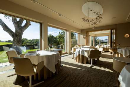 Salle de restaurant lumineuse avec de grandes baies vitrées et des tables élégamment dressées.