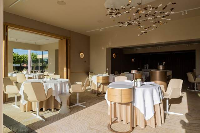 Salle de restaurant lumineuse et moderne, avec des tables rondes et un bar en arrière-plan.